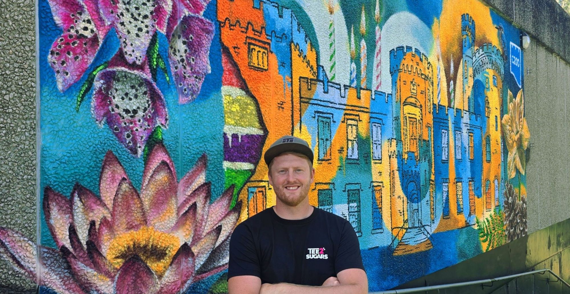 Artist Tee2Sugars stood in front of a colourful mural of Cyfarthfa Castle and large flora and wildlife.jpg Artist Tee2Sugars stood in front of a colourful mural of Cyfarthfa Castle and large flora and wildlife.jpg