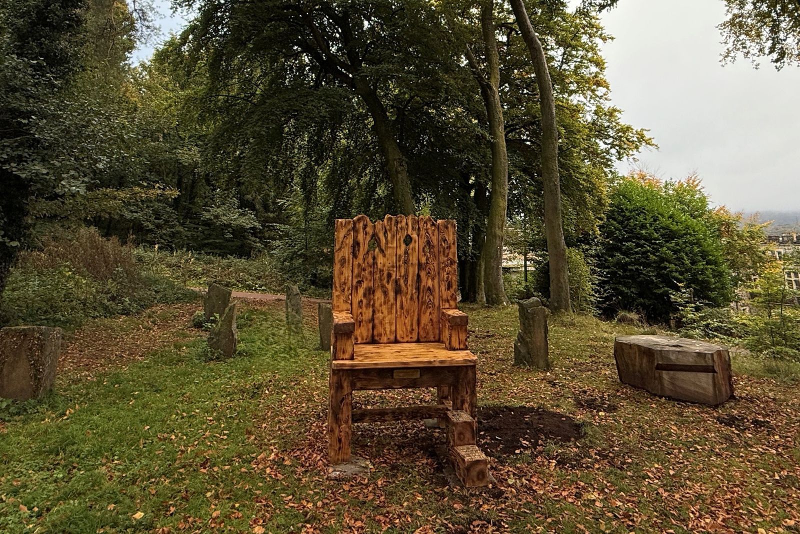 A large wooden chair in a wooded area surrounded by tree stumps and large rocks..jpg