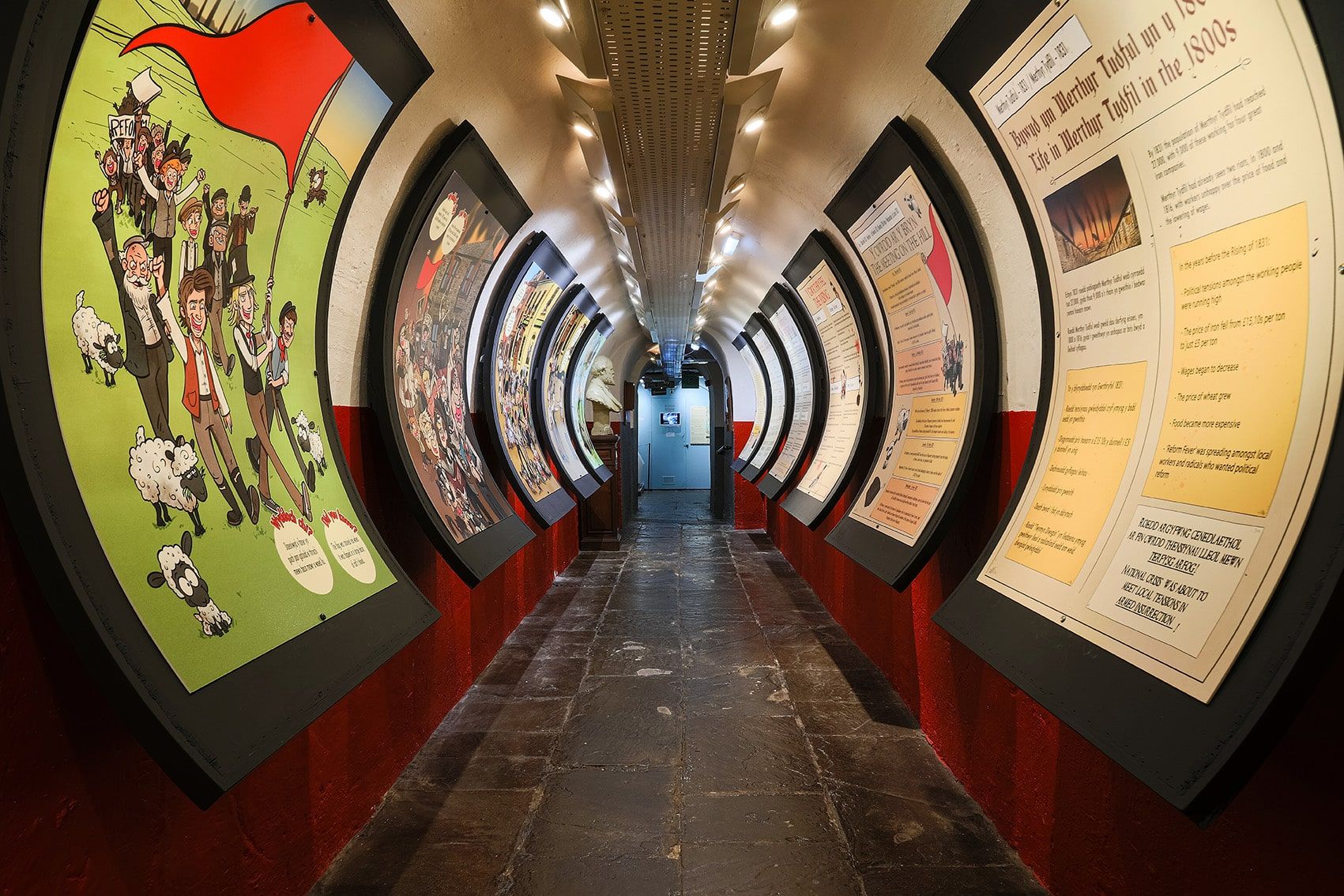 A curved passageway with a black floor and curved displays of information on either side.jpg